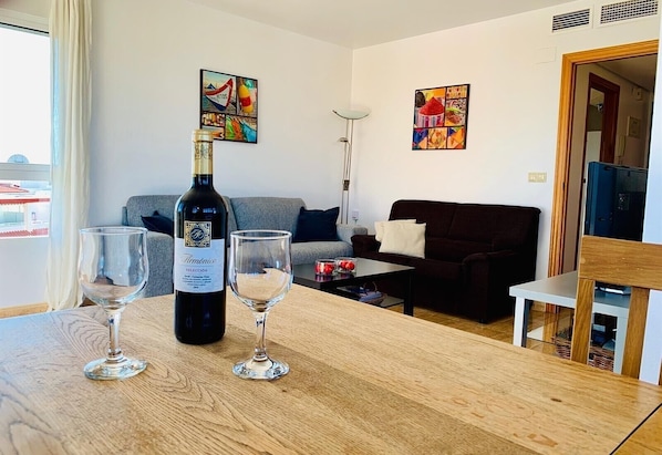 Un salon avec une table en bois, deux verres à vin, une bouteille de vin, un canapé et deux tableaux accrochés au mur.