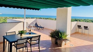Una terraza con una mesa, sillas, una botella de vino y macetas con plantas.