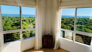 Habitación con dos amplios ventanales que ofrecen vistas a un bosque y al mar.