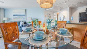 A modern dining area with a glass table, wooden chairs, and a decorative centerpiece. - Make Amazing Maui Memories at 1BD AC - Kaanapali Shores 418 (Lahaina)