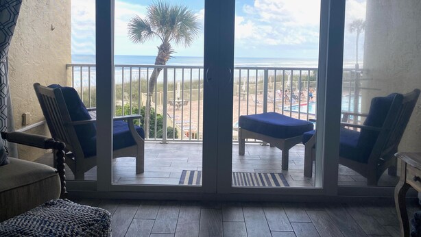 Ein Balkon mit Blick auf den Strand, eine Palme und ein Poolbereich.