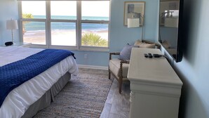 Ein Schlafzimmer mit Bett, Schreibtisch, Stuhl, großem Fenster mit Meerblick und einem Flachbildfernseher.