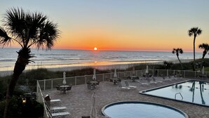 Ein Poolbereich mit Liegestühlen und Sonnenschirmen, mit Blick auf einen Strand bei Sonnenuntergang.