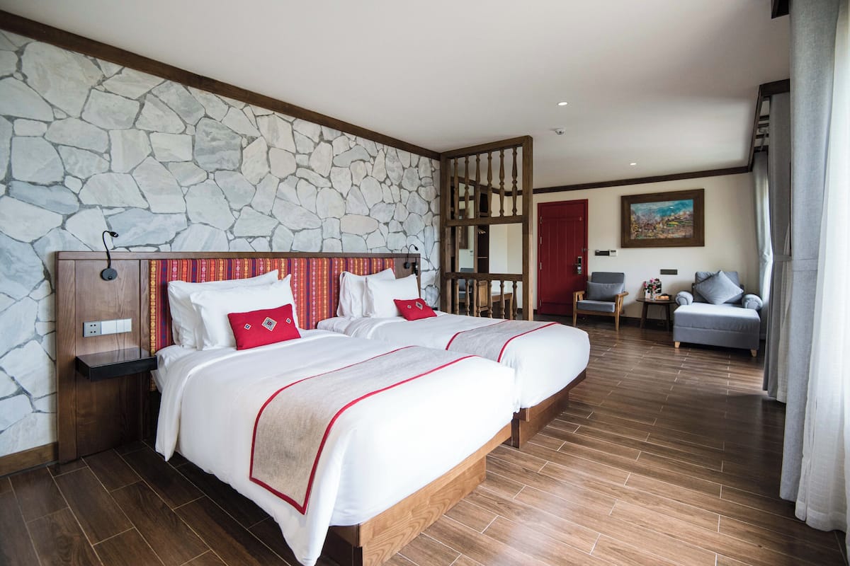 Habitación de hotel con dos camas, pared de piedra, piso de madera, puerta roja y un cuadro en la pared.