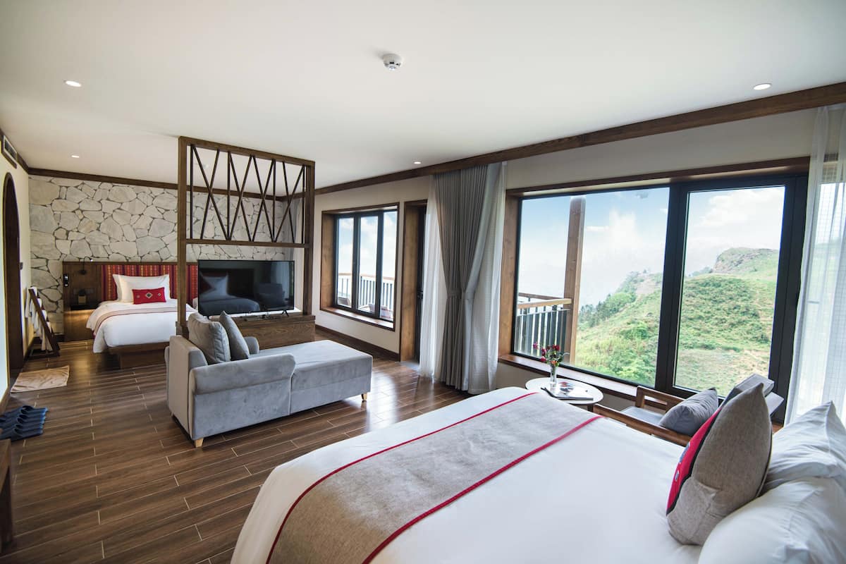 Un dormitorio amplio con una cama grande, un sofá, un televisor y un balcón con vistas panorámicas.