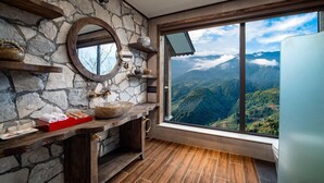 Un baño con paredes de piedra, un tocador de madera, un espejo grande y una ventana con vista a la montaña.