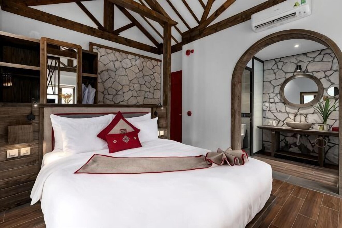 A bedroom with a bed, a stone wall, a mirror, and a wooden ceiling.