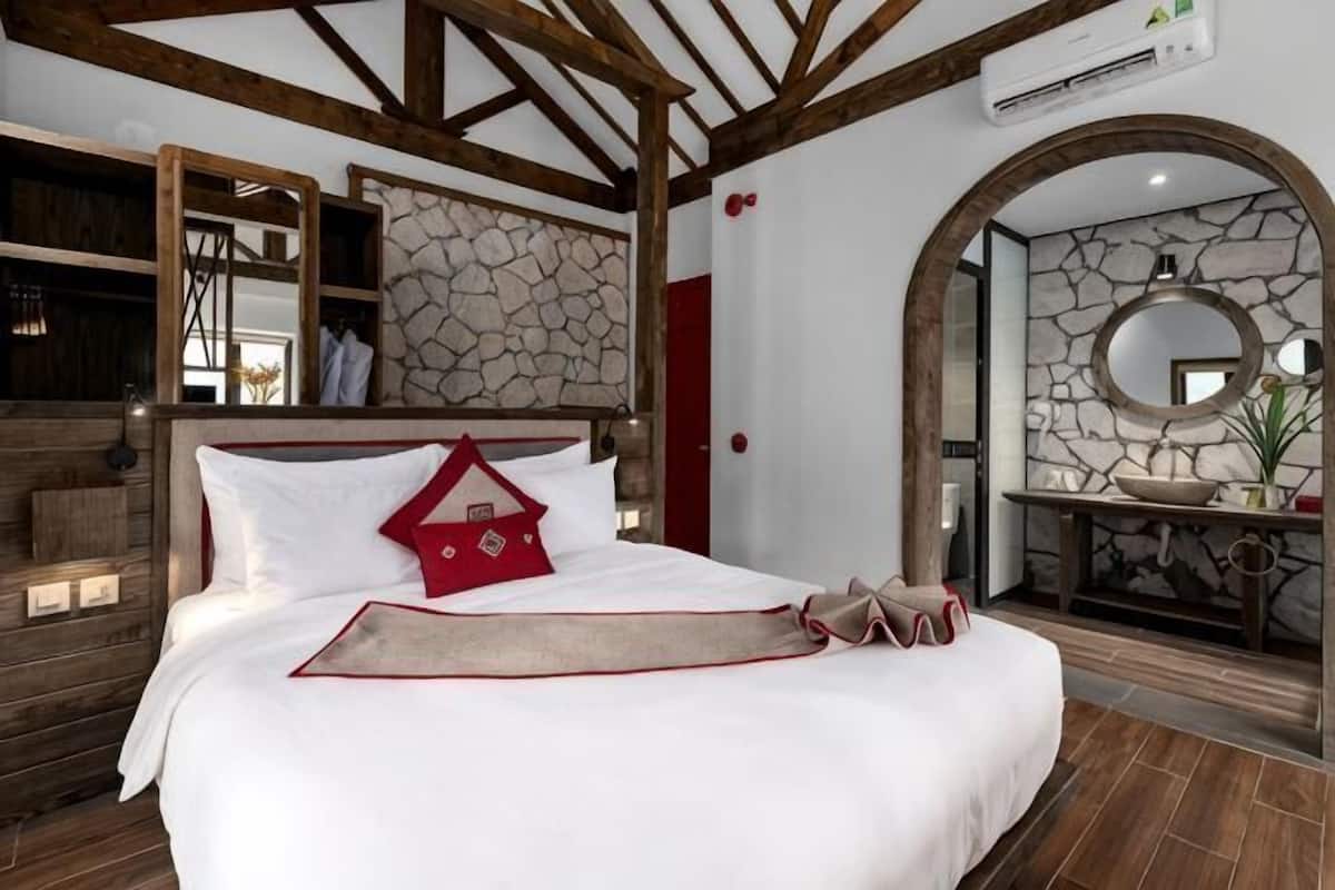 A bedroom with a bed, a stone wall, a mirror, and a wooden ceiling.