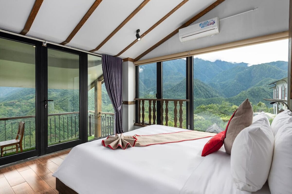 Un dormitorio con una cama grande, vistas a las montañas y un balcón con una silla.