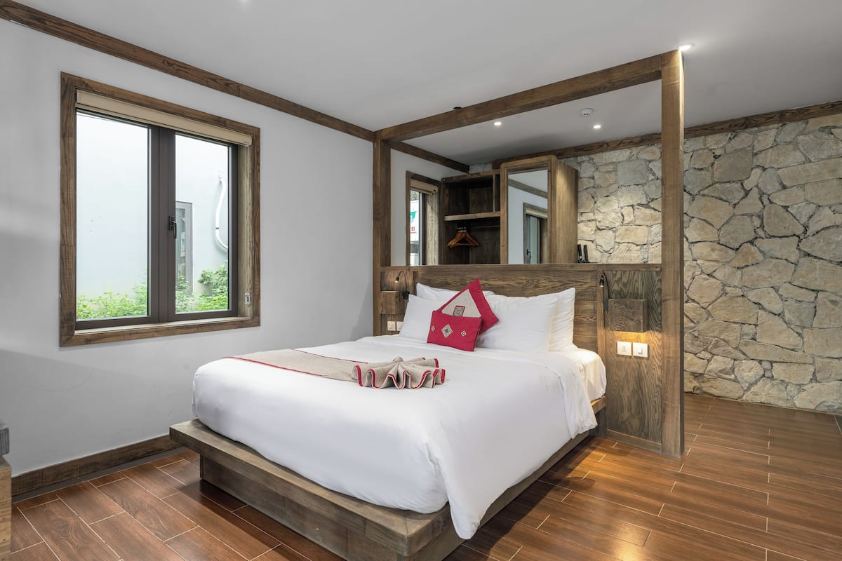 Un dormitorio con un ventanal grande, una pared de piedra y un cabecero de madera.