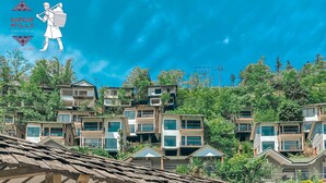 Una mujer descansando en una silla de salón junto a una piscina, con vistas a edificios modernos y vegetación.