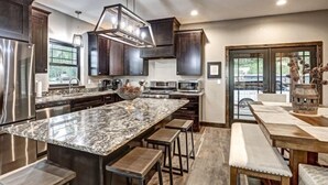 A modern kitchen with dark wood cabinets, stainless steel appliances, a marble island, and a dining area with wooden tables and benches. - Dream Catcher- Spacious Rooms & Views- Sleeps 18 (North Lawrence)