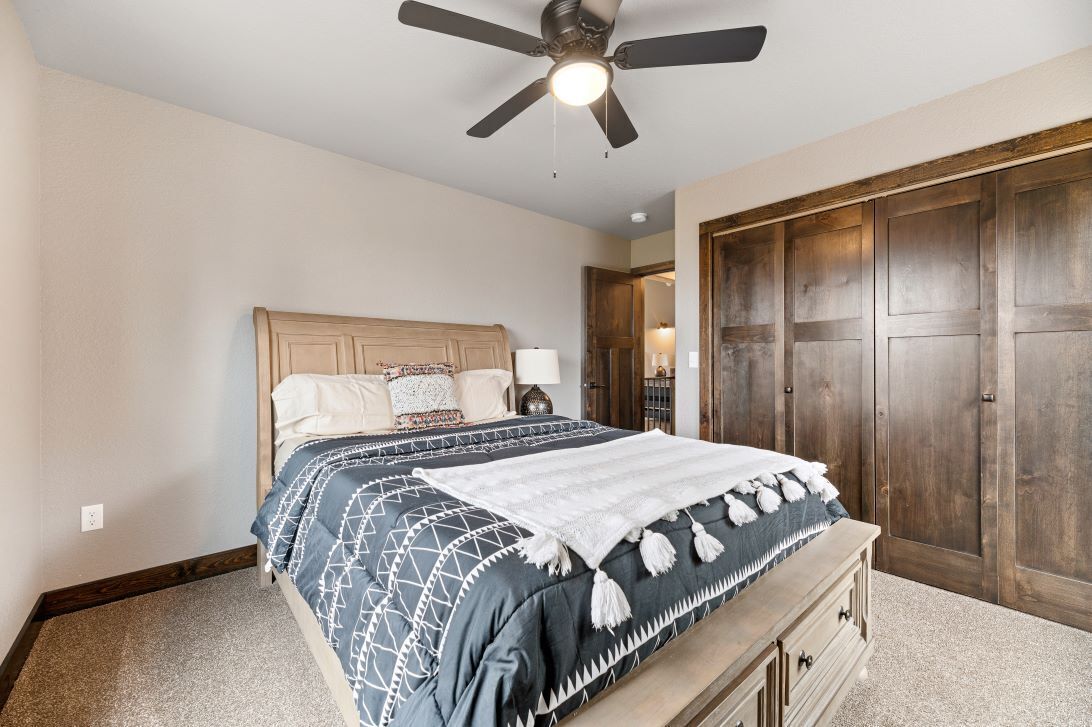 A bedroom with a bed, a ceiling fan, and a wooden wardrobe.