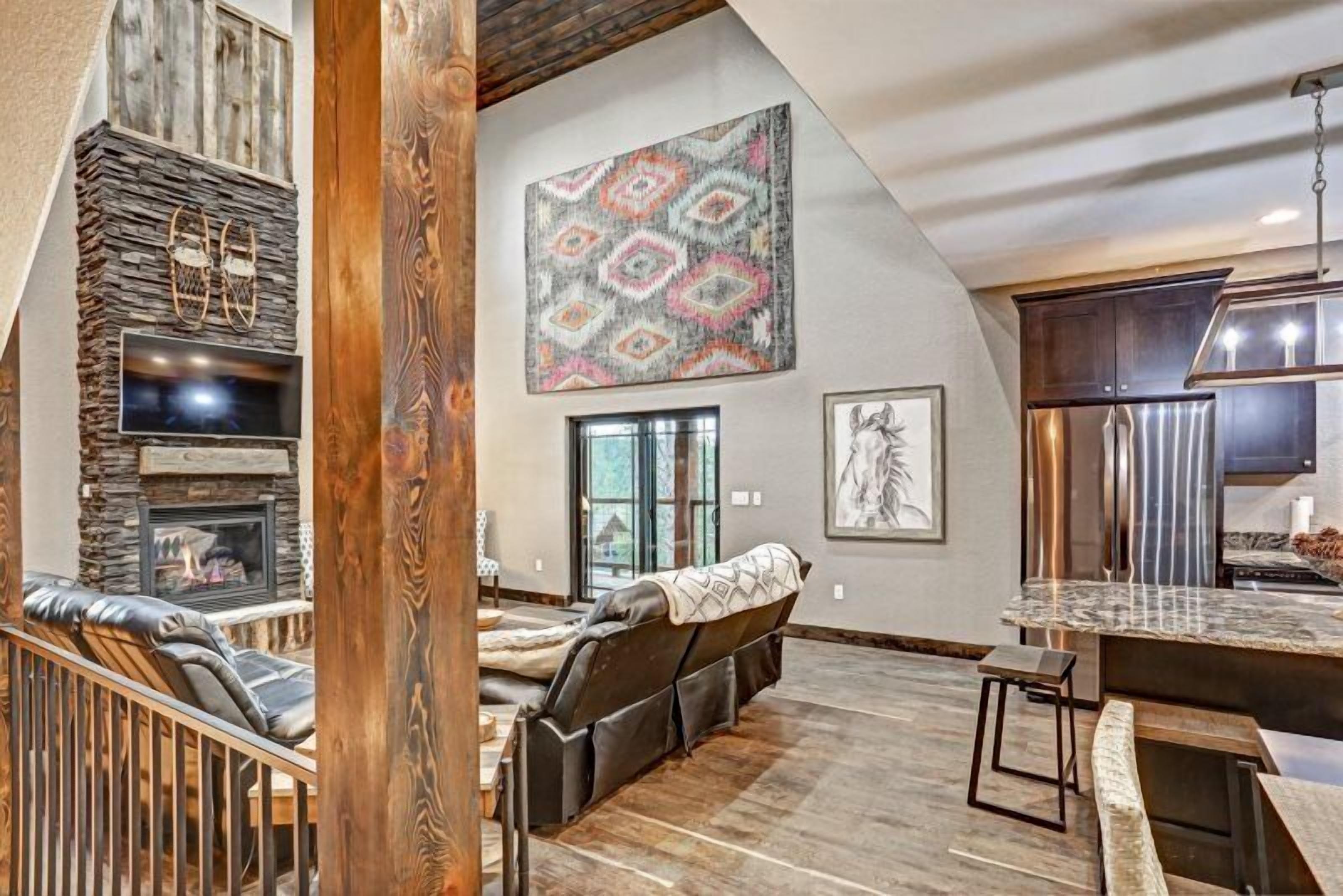 A spacious living area with a stone fireplace, a large wall-mounted artwork, and a modern kitchen with stainless steel appliances.