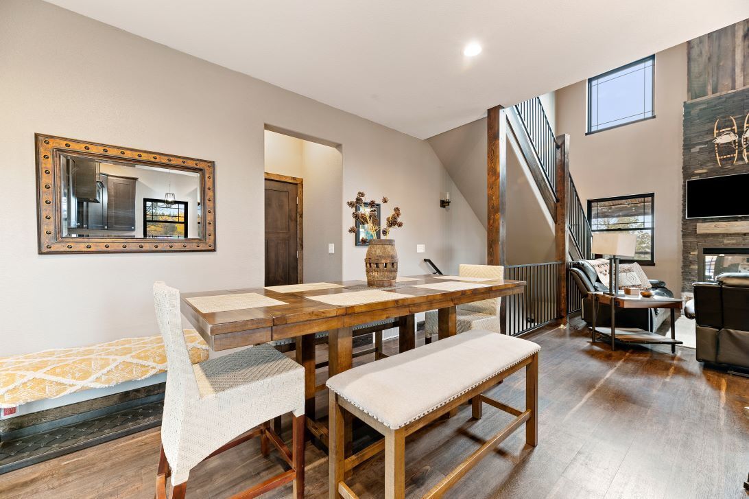 A spacious living area with a wooden dining table, cushioned chairs, a bench, and a staircase leading to an upper level.
