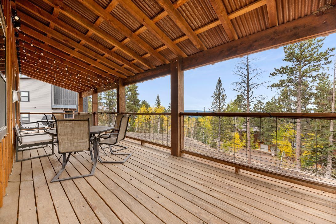 A wooden deck with outdoor furniture, a pergola, and a view of trees and a house.