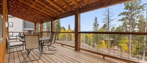 Eine Holzterrasse mit Gartenmöbeln, einer Pergola und Blick auf Bäume und ein Haus.