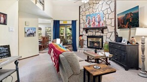Una sala de estar acogedora con chimenea de piedra, un sofá, una mesa de centro y una zona de comedor con cortinas azules.