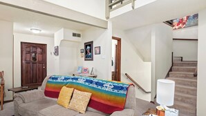 Una sala de estar con un sofá, una puerta de madera, una escalera y un cuadro en la pared.