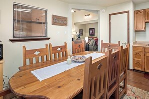 Un comedor con mesa y sillas de madera, una ventana con persianas y una zona de cocina con armarios de madera.
