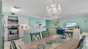 Una cocina moderna con electrodomésticos de acero inoxidable, un comedor con mesa y sillas de madera, y una sala de estar con televisor y obras de arte en la pared.