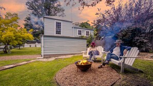A backyard with a fire pit, a house, and a person sitting on a bench. - Pet-Friendly Blue Mountains Cottage with Indoor Fireplace (Mount Victoria)