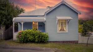 A light blue house with a gabled roof, a porch, and a small garden with pink flowers. - Pet-Friendly Blue Mountains Cottage with Indoor Fireplace (Mount Victoria)
