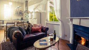 A cozy living room with a leather sofa, a fireplace, and a dining area in the background. - Pet-Friendly Blue Mountains Cottage with Indoor Fireplace (Mount Victoria)
