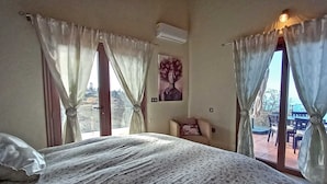 A bedroom with a large bed, a chair, and a view of the outdoors through a window.