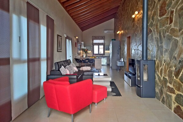 A spacious living area with a modern sofa, a red ottoman, and a stone fireplace.