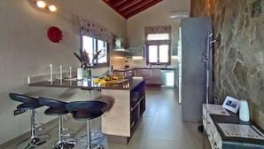 A modern kitchen with a central island, bar stools, and a stone accent wall.