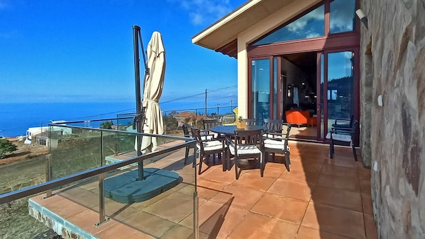 A balcony with outdoor furniture, a glass door leading inside, and a view of the ocean.