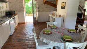 A kitchen with a dining table set for four, white chairs, and a staircase leading to an upper level. - Holiday Home in Chilleurs near Château (Chilleurs-aux-Bois)
