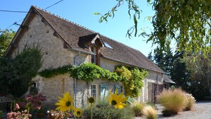 A stone building with a sloped roof, surrounded by a gravel driveway and various plants. - Holiday Home in Chilleurs near Château (Chilleurs-aux-Bois)