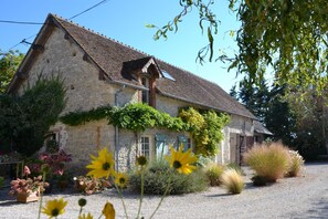Surrounded by a well-maintained garden, this charming residence features a traditional stone building with a sloped roof and a small window with shutters.