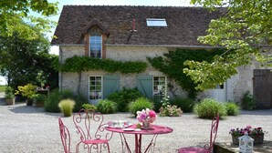 A rustic stone building with a tiled roof, surrounded by a gravel courtyard with red metal chairs and a table. - Holiday Home in Chilleurs near Château (Chilleurs-aux-Bois)