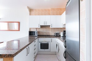 Cocina compacta con armarios blancos, encimera de granito, microondas, tostadora, cafetera, horno y lavadora.