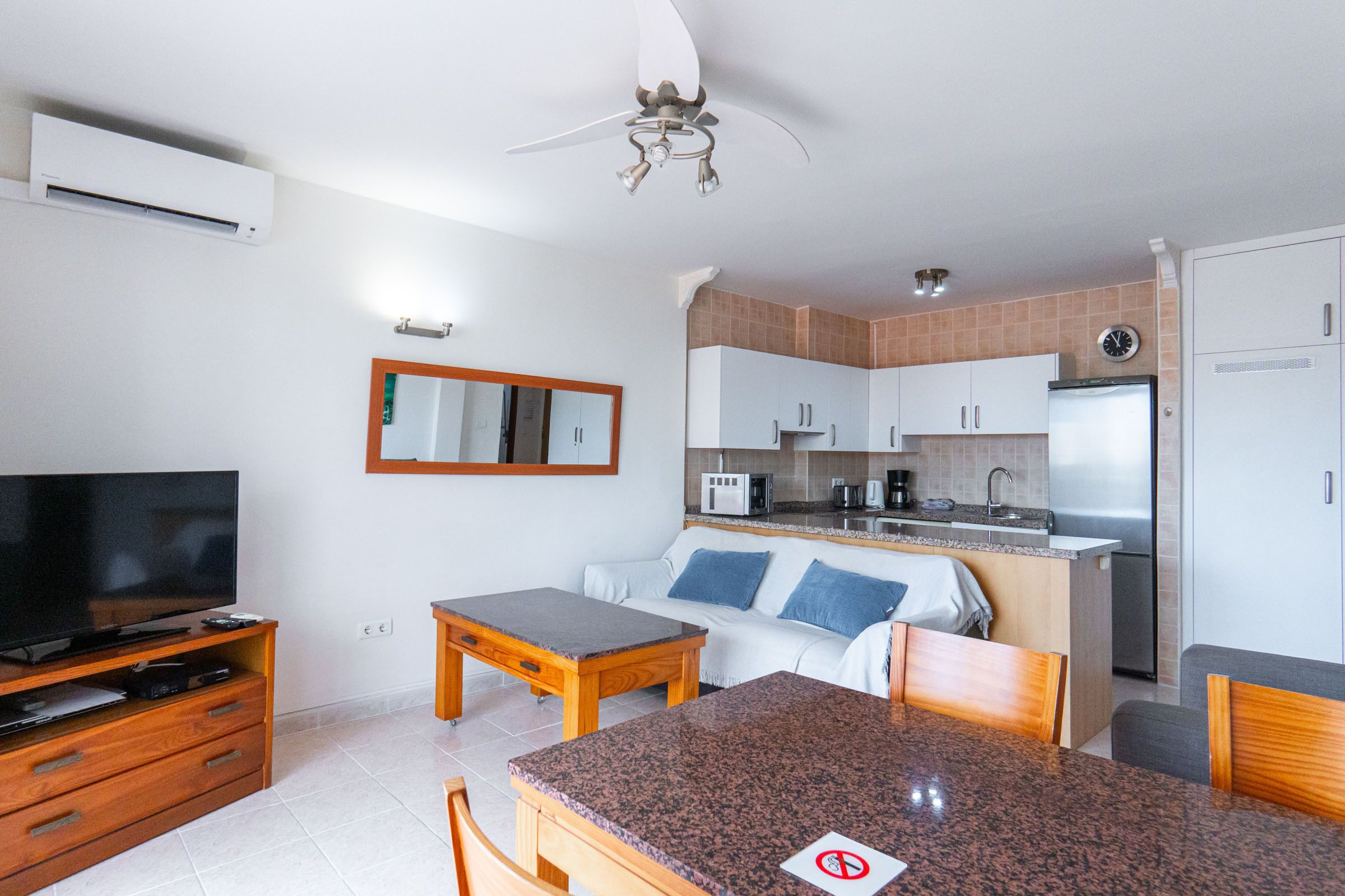 A compact living space with a kitchenette, a dining area, a television, and a ceiling fan.