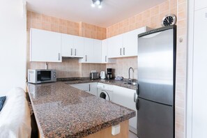 A compact kitchen with white cabinets, a stainless steel refrigerator, a microwave, a toaster, and a washing machine. - Torresol Torrecilla 506 by Casasol (Nerja)