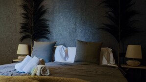 Una cama bien hecha con almohadas, una manta y toallas enrolladas. Hay dos mesitas de noche con lámparas.