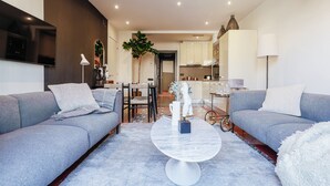 Una sala de estar moderna con sofás grises, una mesa de centro de mármol y un comedor con una planta y una pequeña mesa.