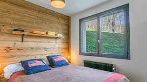 Een slaapkamer met een houten hoofdbord, een groot raam met uitzicht op bomen, en twee kussens met een ontwerp van de Amerikaanse vlag.