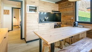 Een moderne keuken met houten kastjes, een centraal kookeiland met krukken, een inbouwoven en een groot raam met uitzicht op de omgeving.