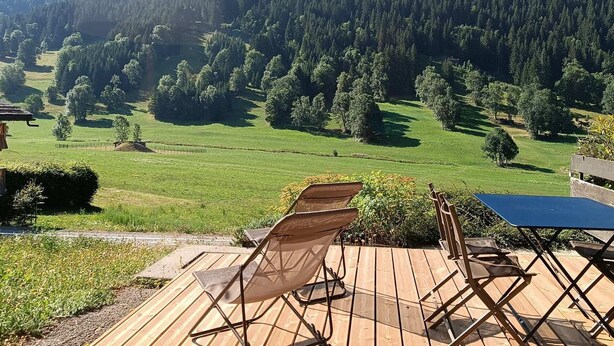 Een terras met stoelen en een tafel, met uitzicht op een bergachtig landschap met dichte bossen.