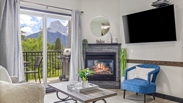 Un salon avec une cheminée, un tél éviseur fixé au mur et un balcon offrant une vue sur la montagne.