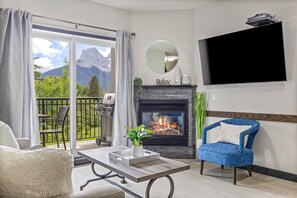 Un soggiorno con camino, TV a parete e un balcone con vista sulle montagne.
