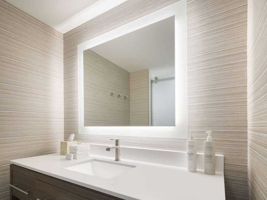 A modern bathroom with a large mirror, white sink, and wooden vanity.