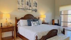 A bedroom with a wooden bed, two bedside tables, a bench, and three paintings on the wall.