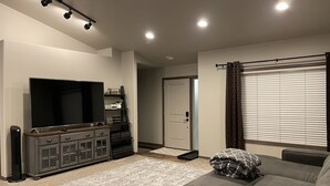 A living room with a flat-screen TV, a dark wooden cabinet, a gray sofa, and a patterned rug. - Cozy 4King bed+3Bath near Downtown&Airport open concept Scenic backyard view (Sioux Falls)