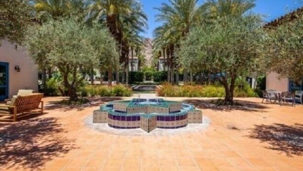 Un patio con una piscina central, rodeado de palmeras y un edificio con una puerta azul.